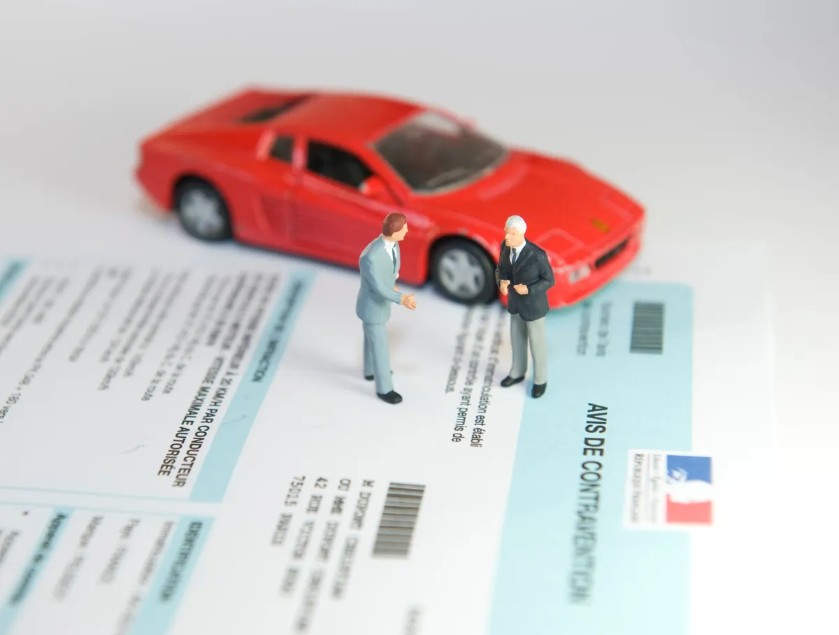 Image de figurines symbolisant une consultation juridique en droit routier, avec une voiture rouge en arrière-plan et un avis de contravention.